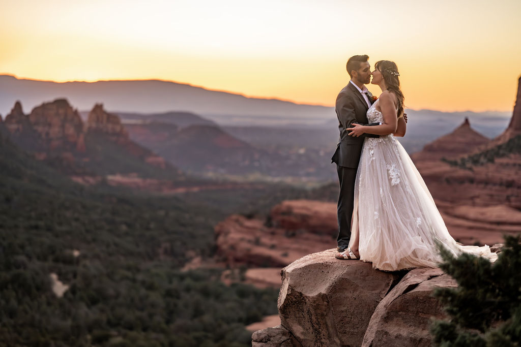 couple kiss while standing on ledge during sunrise after sedona alternative wedding