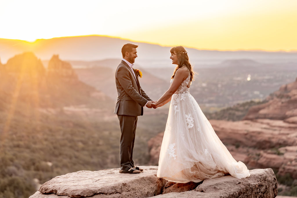 couple holding hands while standing on ledge during sunrise after sedona alternative wedding