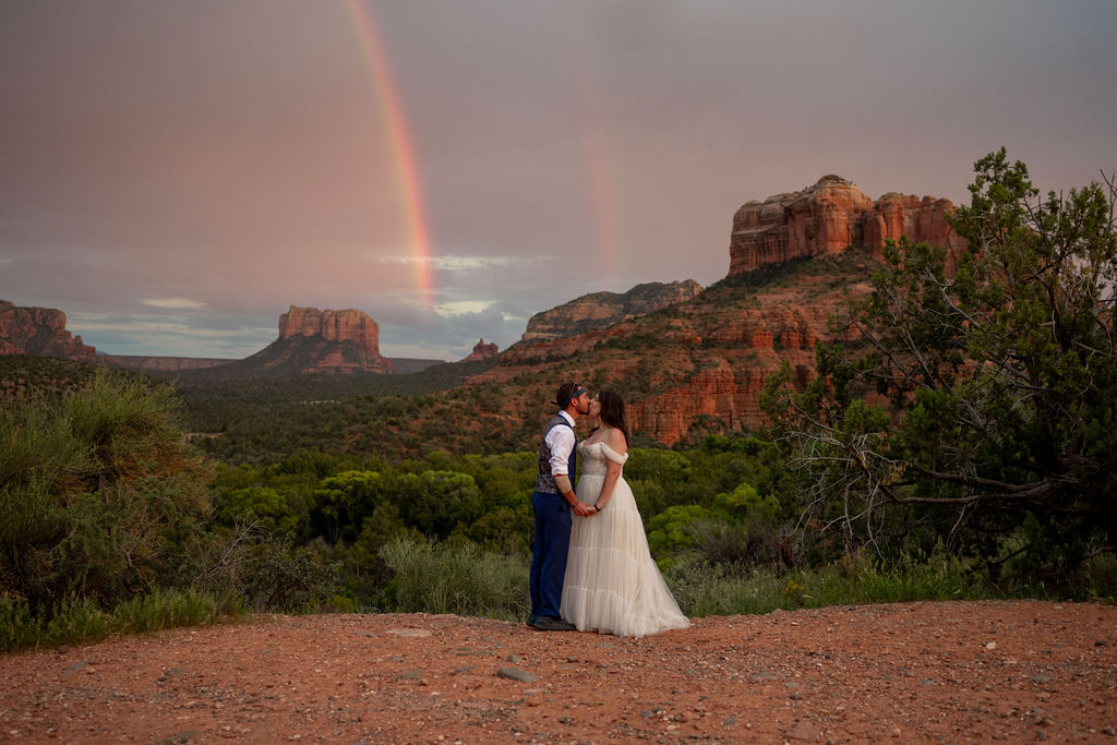 couple kiss with rainbow and red rock formations in the background