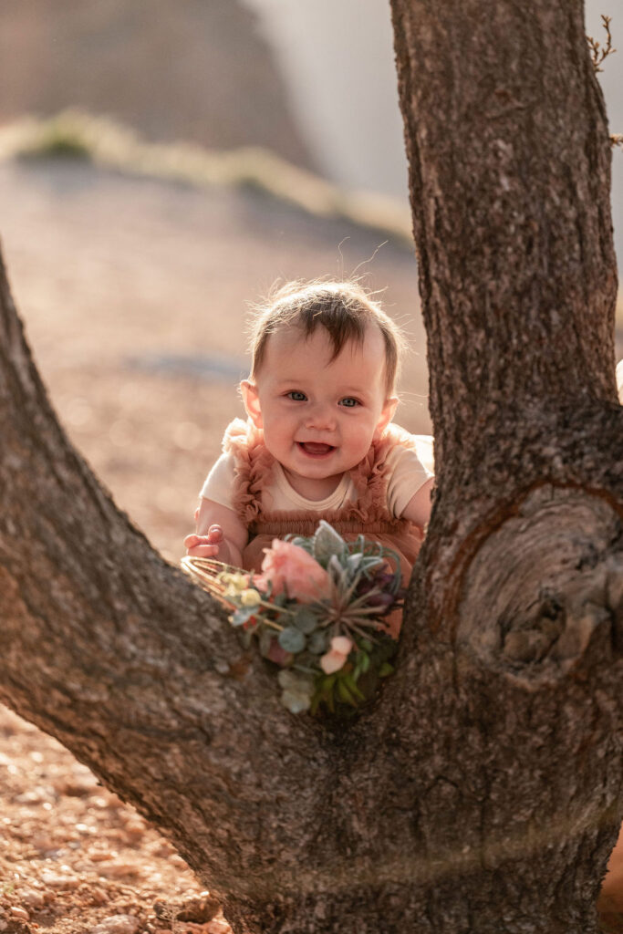 couple's 9 month old daughter smiling behind tree