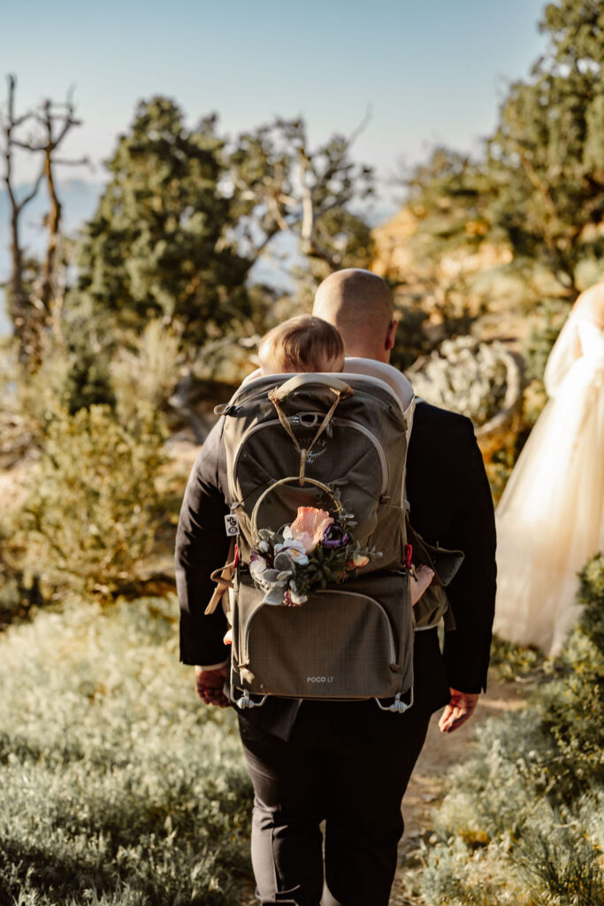 groom carrying daughter in backpack carrier during hike