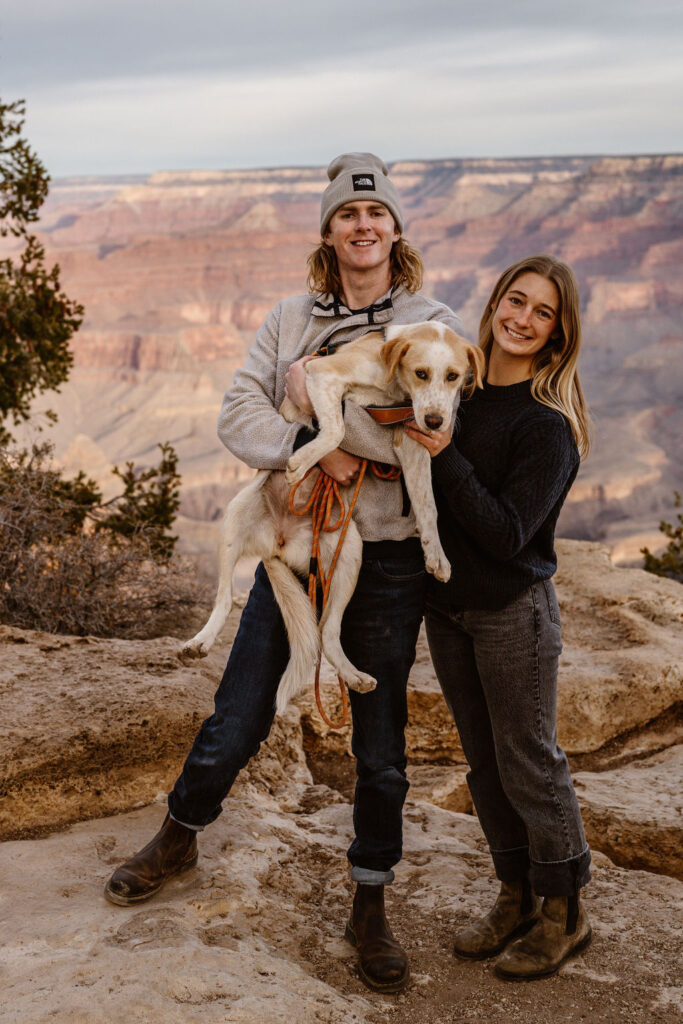 couple holding their dog at rocky ledge of Grand Canyon