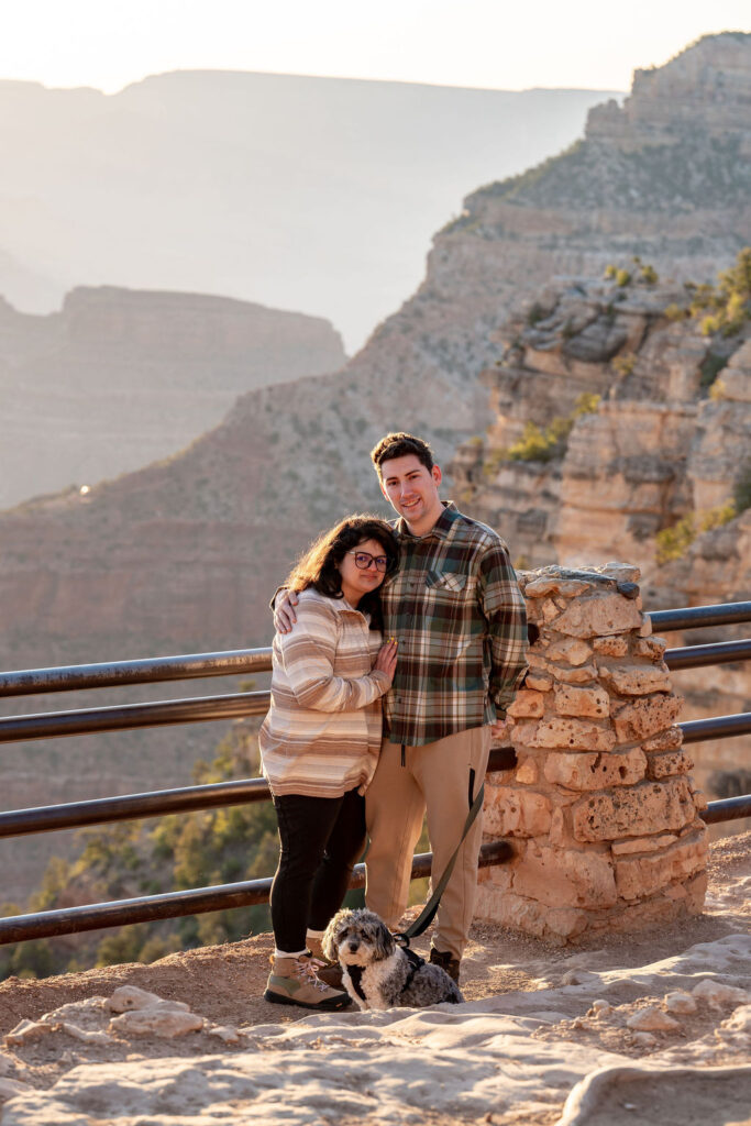 couple stands in front of railing with their dog 