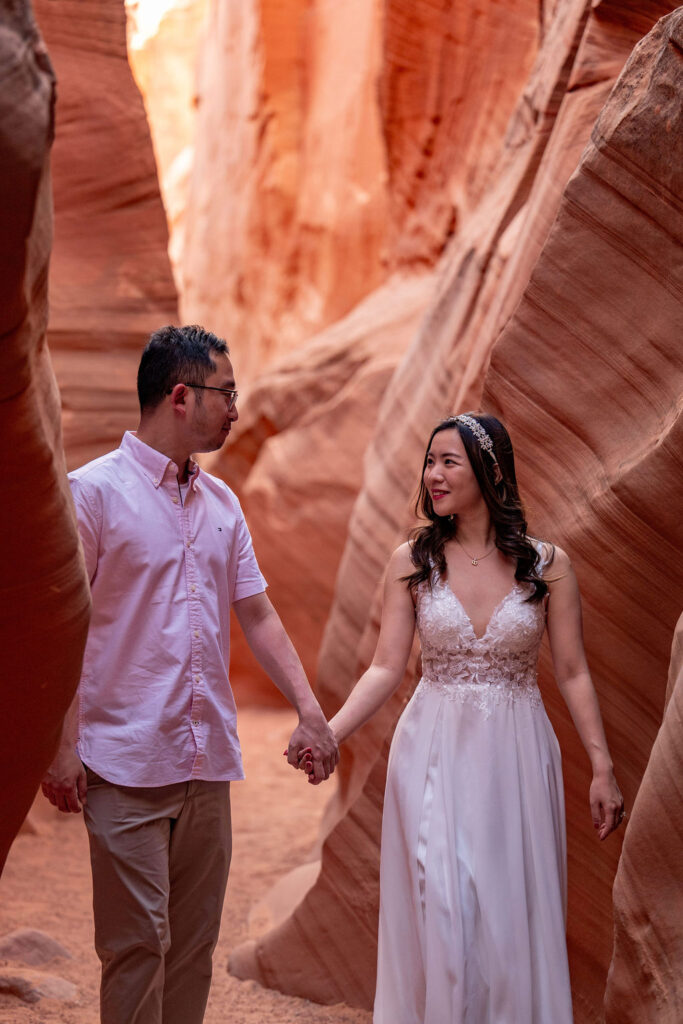 couple walks through red rock structures in Antelope Canyon