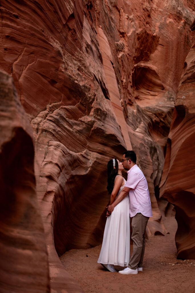 couple embrace along red rock structures in Antelope Canyon