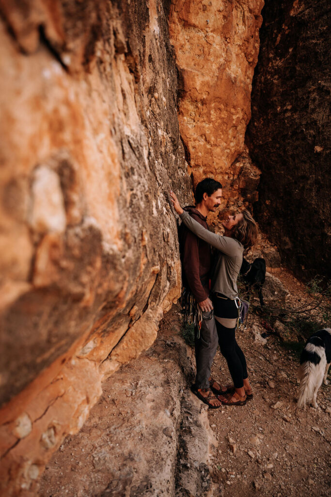 couple embrace against rock in all their rock climbing gear