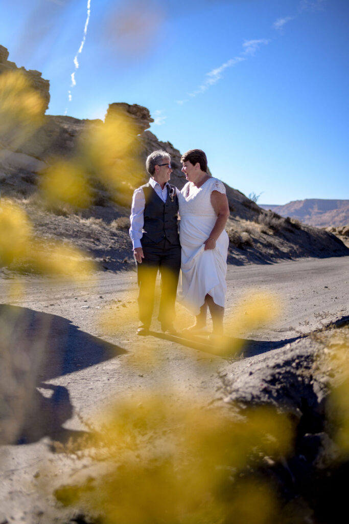 couple laugh together as they pose on dirt road with rocky landscape in the background