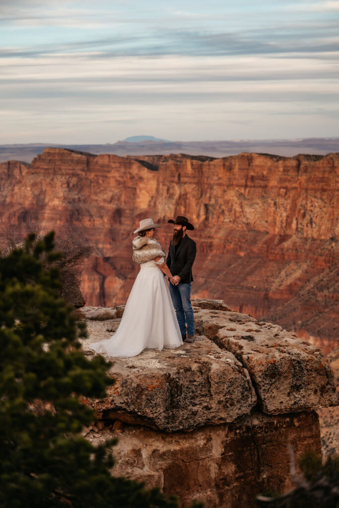 couple holding hands standing on ledge overlooking the Grand Canyon