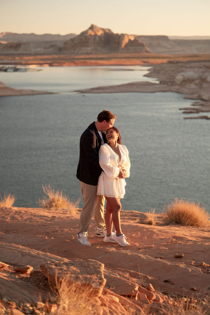 couple embrace in the sand by the water