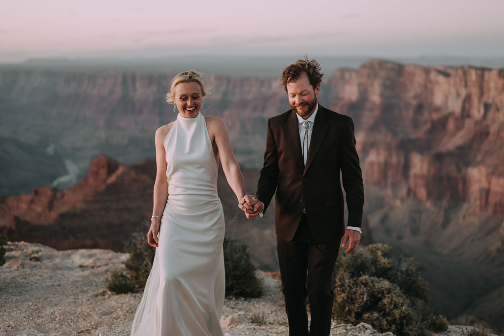 couple hold hands and walk along edge during Grand Canyon adventure