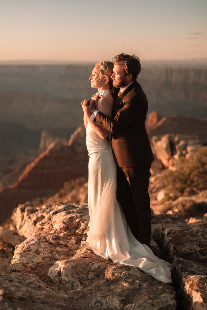 couple embrace as they overlook the Grand Canyon during sunset