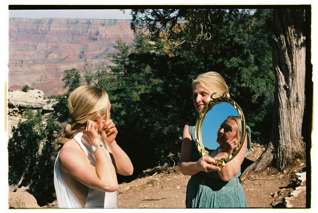 bride putting in earrings while looking in mirror