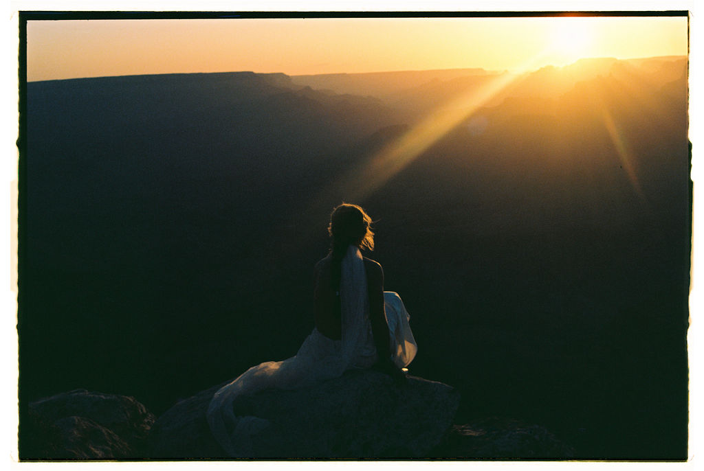 Bride sitting on ledge at sunset