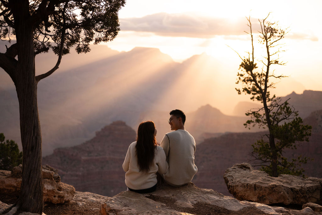couple sits on cliff edge at grand canyon sunset